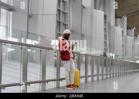 African American young man using smartphone travelling with luggage inside in airport terminal  Stock Photo