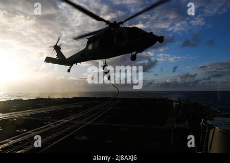 PHILIPPINE SEA (May 11, 2022) Explosive Ordnance Disposal 2nd Class Cole Adey, from Akron, Ohio, assigned to Explosive Ordnance Disposal Mobile Unit (EODMU) 3, ropes down from an MH-60S Sea Hawk helicopter, assigned to the “Chargers” of Helicopter Sea Combat Squadron (HSC) 14 onto the Ticonderoga-class guided-missile cruiser USS Mobile Bay (CG 53) during a helicopter visit, board, search and seizure (HVBSS) training. Abraham Lincoln Strike Group is on a scheduled deployment in the U.S. 7th Fleet area of operations to enhance interoperability through alliances and partnerships while serving as Stock Photo