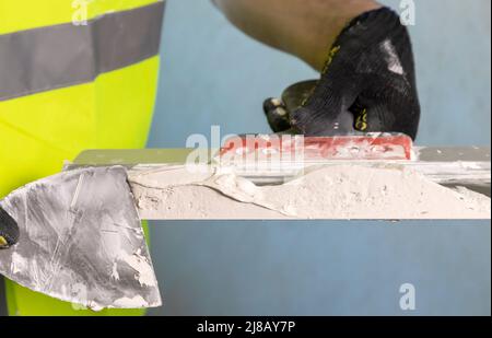 Close up of the master mixes the plaster mixture on a spatula for application to the wall. Stock Photo