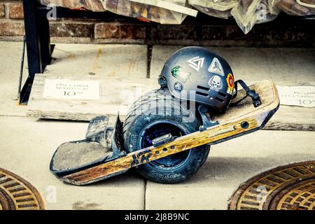 04 15 2022 Tulsa USA - Well used and slightly battered  one wheel electric skateboard with helmet covered with stickers parked on sidewalk outside gro Stock Photo