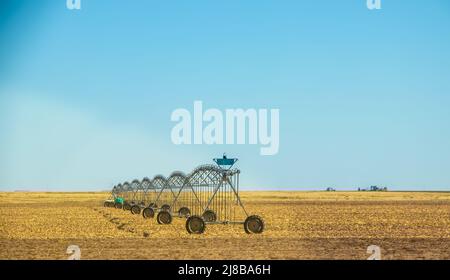 Irrigation system on wheels sitting in flat brown agricultural field under clear blue sky Stock Photo