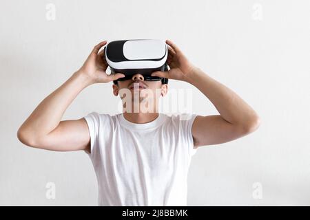 Young man wearing virtual reality goggles headset on gray background. Concept of VR, video game, future, gadgets and technology. Stock Photo