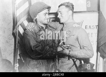 An American soldier (2nd Lt. William Robertson, US Army) and a Red Army soldier (Lt. Alexander Sylvashko, Red Army) meeting during the allied invasion of Germany. The photo is a staged propaganda piece, with the nations flags and the East Meets West sign behind. Stock Photo
