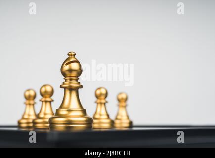 The golden bishop chess piece in front gold pawns on white background with copy space. Bishop represents the church, important and powerful entity thr Stock Photo