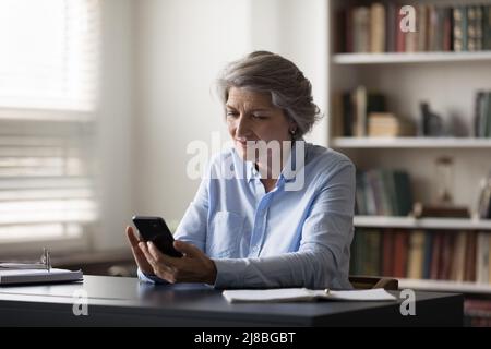 Positive grey haired business woman using smart online app Stock Photo
