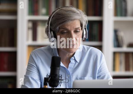 Serious newscaster, radio host in headphones speaking at professional microphone Stock Photo