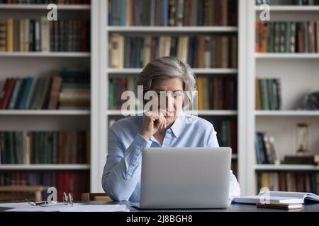 Positive focused senior business lady using laptop at table Stock Photo