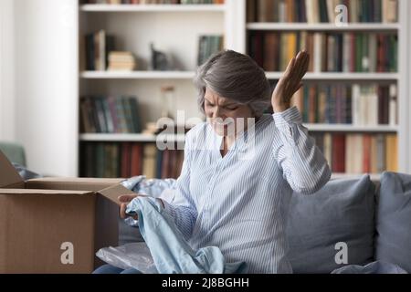 Angry frustrated senior customer woman receiving parcel with damaged goods Stock Photo