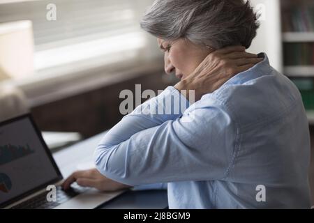 Upset stressed mature woman suffering from neck ache Stock Photo