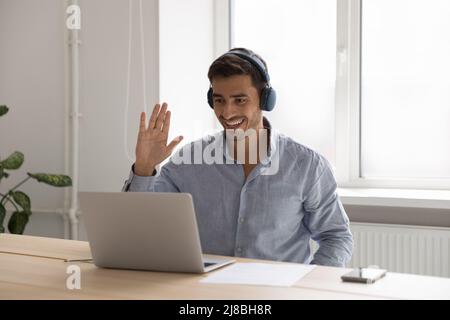 Happy millennial entrepreneur man in headphones waving hand hello Stock Photo