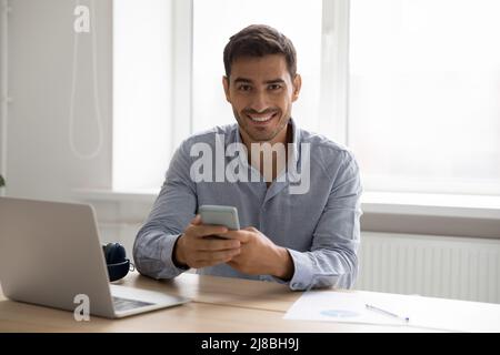 Happy gadgets user man using smartphone, laptop at home workplace Stock Photo