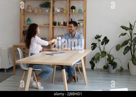 Happy coworkers shaking hands over table due to completing project Stock Photo