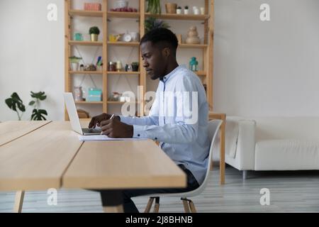 Serious busy African freelance employee writing in paper document Stock Photo