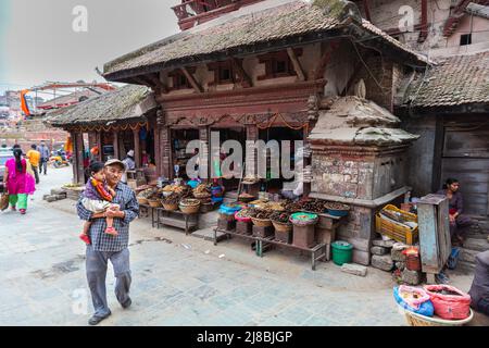 Kathmandu, Nepal - October 27, 2021: A man with a child in his arms stands in front of a shop on the Durbar square in the capitol of Nepal. Dried fish Stock Photo