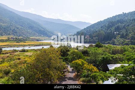 Wide angle panorama over the free wild open landscape of Bhutan. The mountain of the Himalayas in the haze on the horizon. A river meanders through th Stock Photo
