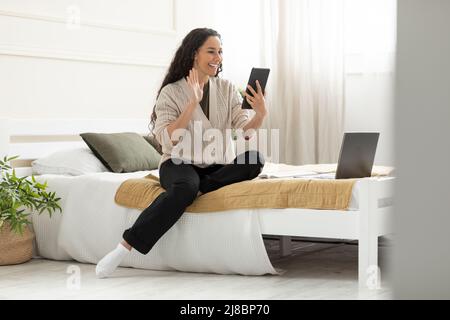 Smiling young woman waving hand using digital tablet Stock Photo