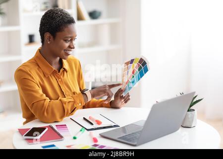 Smiling black woman working as web designer, office interior Stock Photo
