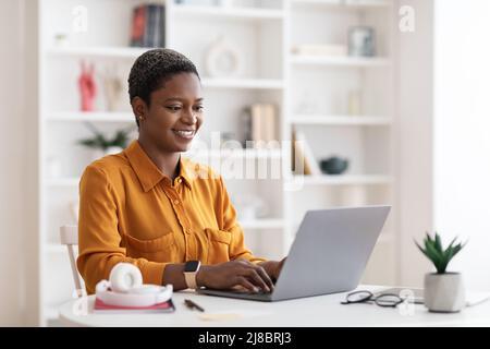 Happy african american lady freelancer using laptop at home Stock Photo