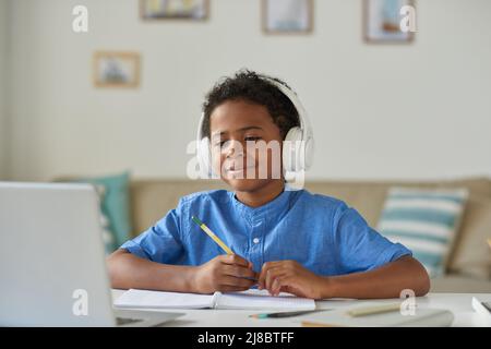 Content curious African-American boy in wireless headphones using laptop while talking to tutor via video conferencing app Stock Photo