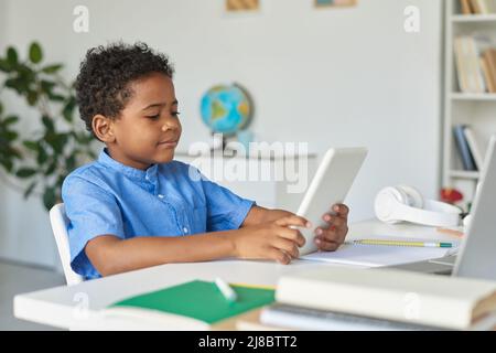 Modern African American schoolboy sitting at desk and using tablet for education at home Stock Photo