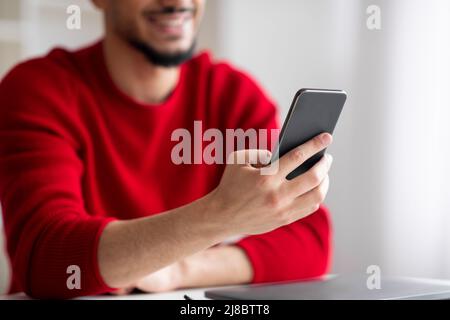 Cropped smiling young islamic man with beard typing on smartphone in home office interior Stock Photo