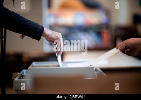 15 May 2022, North Rhine-Westphalia, Essen: A woman throws her ballot paper into a ballot box at a polling station in Essen. Photo: Fabian Strauch/dpa Stock Photo