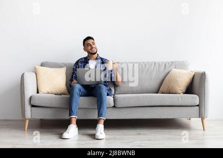Man using pc sitting on the couch, drinking coffee Stock Photo