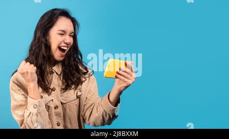 Glad happy young european brunette woman in casual looking at smartphone and make winning gesture Stock Photo