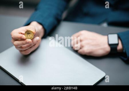 Businessman in suit with smartwatch holds bitcoin in his hand in office interior, cropped Stock Photo