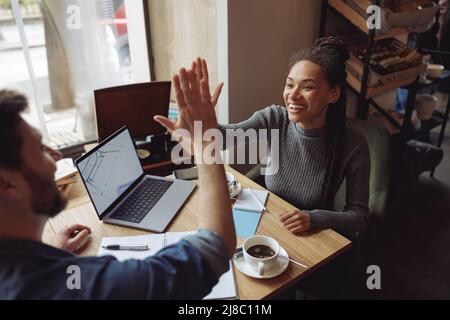 Happy friends startupers giving high five, working on partnership in cafe. Sharing same vision. Stock Photo