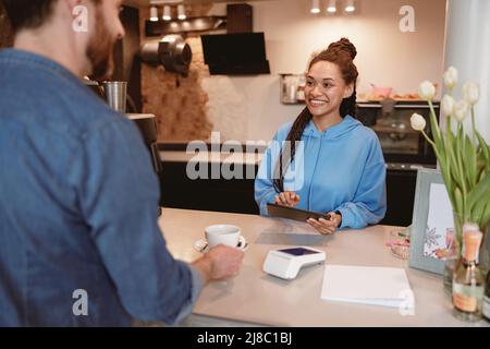 Back view on man client at cafeteria counter taking away cup of coffee. Female barista serving. Stock Photo