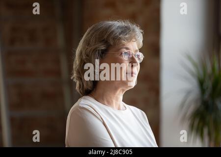 Mature woman in glasses standing indoor staring into distance Stock Photo