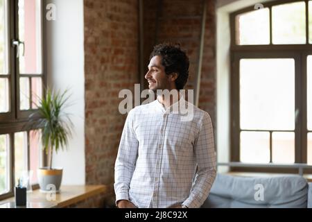 Hispanic man standing in loft apartment smiling staring out window Stock Photo