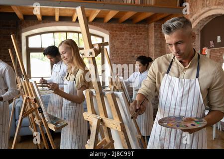 Handsome millennial painter man painting during group art-class Stock Photo