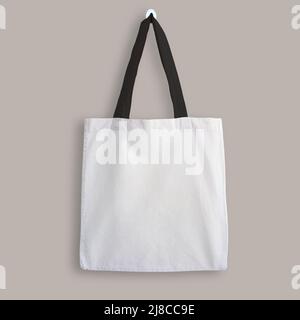 White blank cotton eco tote bag with black straps, design mockup. Shopping bag hanging on wall Stock Photo