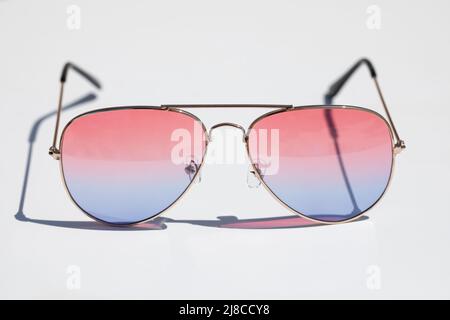 Sunglasses with pink and blue lenses on a white surface. Illuminated by strong sunlight. Vacation and well-being concept. Stock Photo