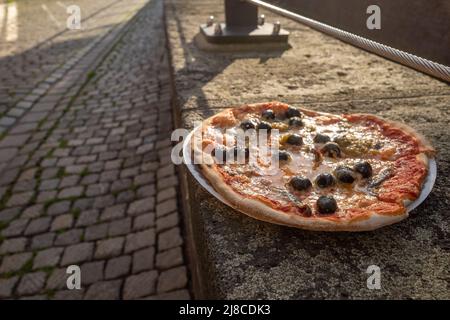 Pizza napoli style with olive and anchovy fish leave on stone fence beside canal in old town in Europe. Stock Photo