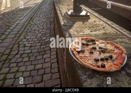 Pizza napoli style with olive and anchovy fish leave on stone fence beside canal in old town in Europe. Stock Photo