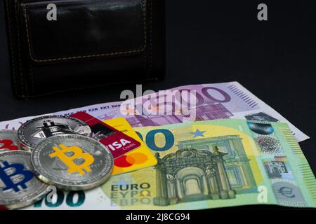 Golden Bitcoin coins lied on top of 100 Euros and 500 Euros bank notes and credit cards. Gold bitcoin on one hundred and five hundred euros banknotes. Stock Photo