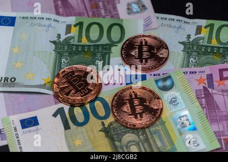 Golden Bitcoin coins lied on top of 100 Euros and 500 Euros bank notes. Gold bitcoin on one hundred and five hundred euros banknotes. Stock Photo