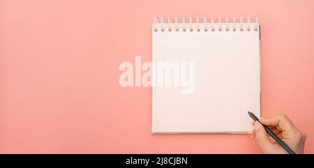 writing in blank notepad on pink background. female hands writing in mockup notepad. Woman writing in notepad. Mockup notepad with woman hands on pink Stock Photo