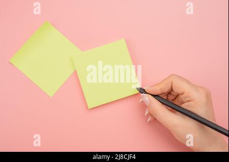 Hand written notes black pencil on yellow sticker. pink table background. woman hand writing on yellow sticky notes. Business people meeting and use n Stock Photo