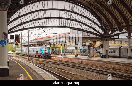 Trains stand beside a hitorical canopy viewed from under an arch. Columns are in the foreground. Stock Photo