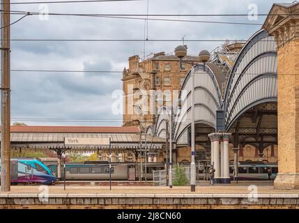 Historic arches are over the entrance to a railway station. Trains stand at platforms and a cloudy sky is above. Stock Photo