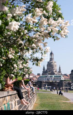 15 May 2022, Saxony, Dresden: Passers-by sit on a wall on the banks of the Elbe River in front of the backdrop of the Frauenkirche church. Photo: Sebastian Kahnert/dpa