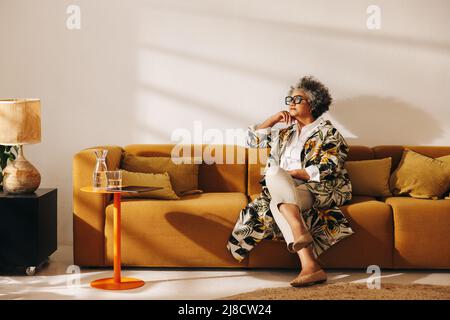 Mature businesswoman looking away thoughtfully while sitting on a couch in an office lobby. Experienced businesswoman working in a creative coworking Stock Photo