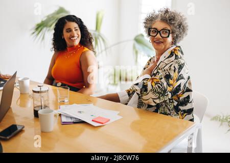 Happy businesswomen smiling cheerfully while sitting in a boardroom meeting. Diverse businesswomen working as a team in an all-female startup. Stock Photo