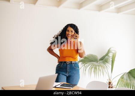 Female entrepreneur smiling happily while speaking with her business partners on a phone call. Cheerful young businesswoman making business plans whil Stock Photo