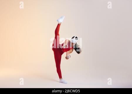 Young woman playing a virtual fitness game using gaming controllers. Active young woman stretching her leg while working out in virtual reality. Woman Stock Photo