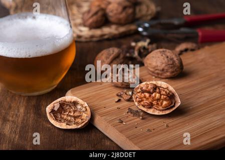 Cracked walnuts on a wooden board next to a glass of beer. Stock Photo